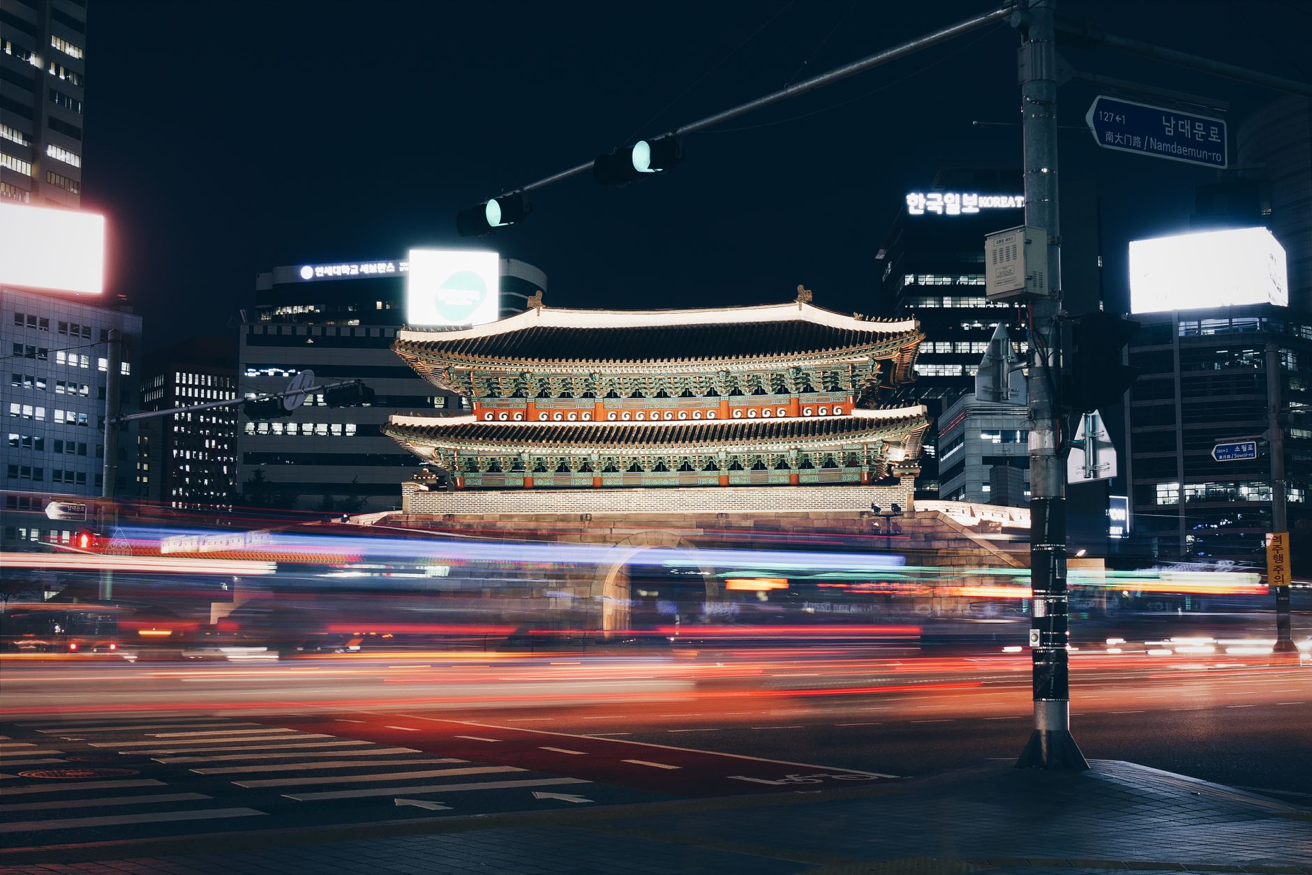 Nighttime long exposure of Seoul's Namdaemun Gate with city lights and traffic motion blur.