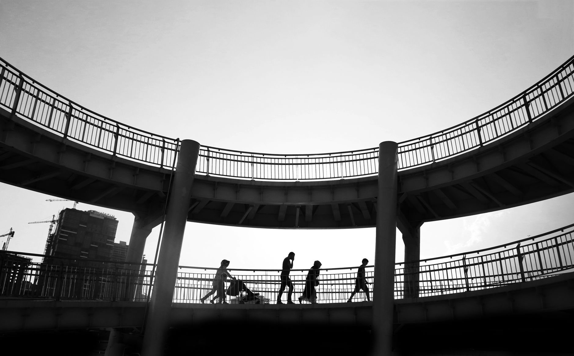 Silhouettes of people walking on an elevated urban walkway under clear skies.