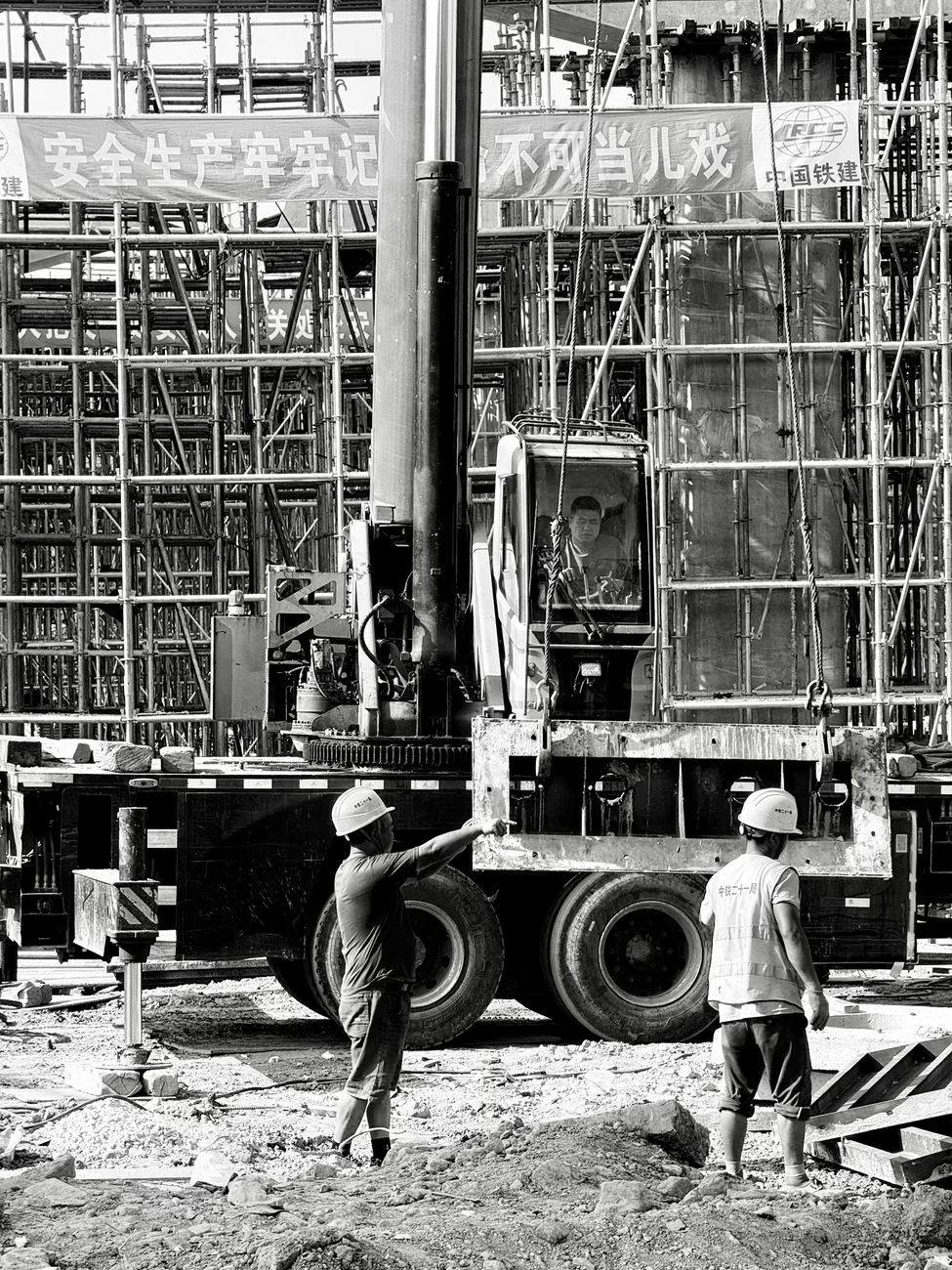 Black and white image showing construction workers and equipment on a busy building site in Shanghai.