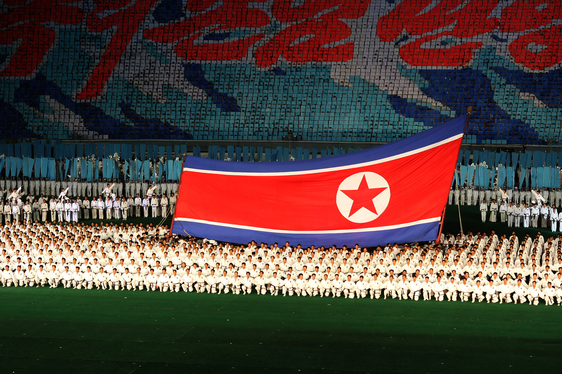 Young men in Taekwondo outfits carry a large North Korean flag during Arirang Mass Games