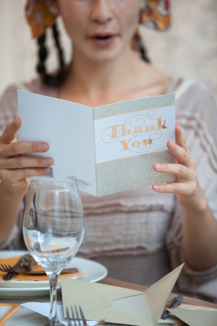 A woman reads a thank you card at a warmly decorated, festive dinner table.