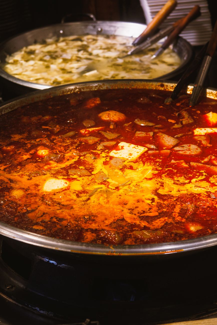 Close-up of a spicy red hot pot dish served in a large metal bowl indoors.