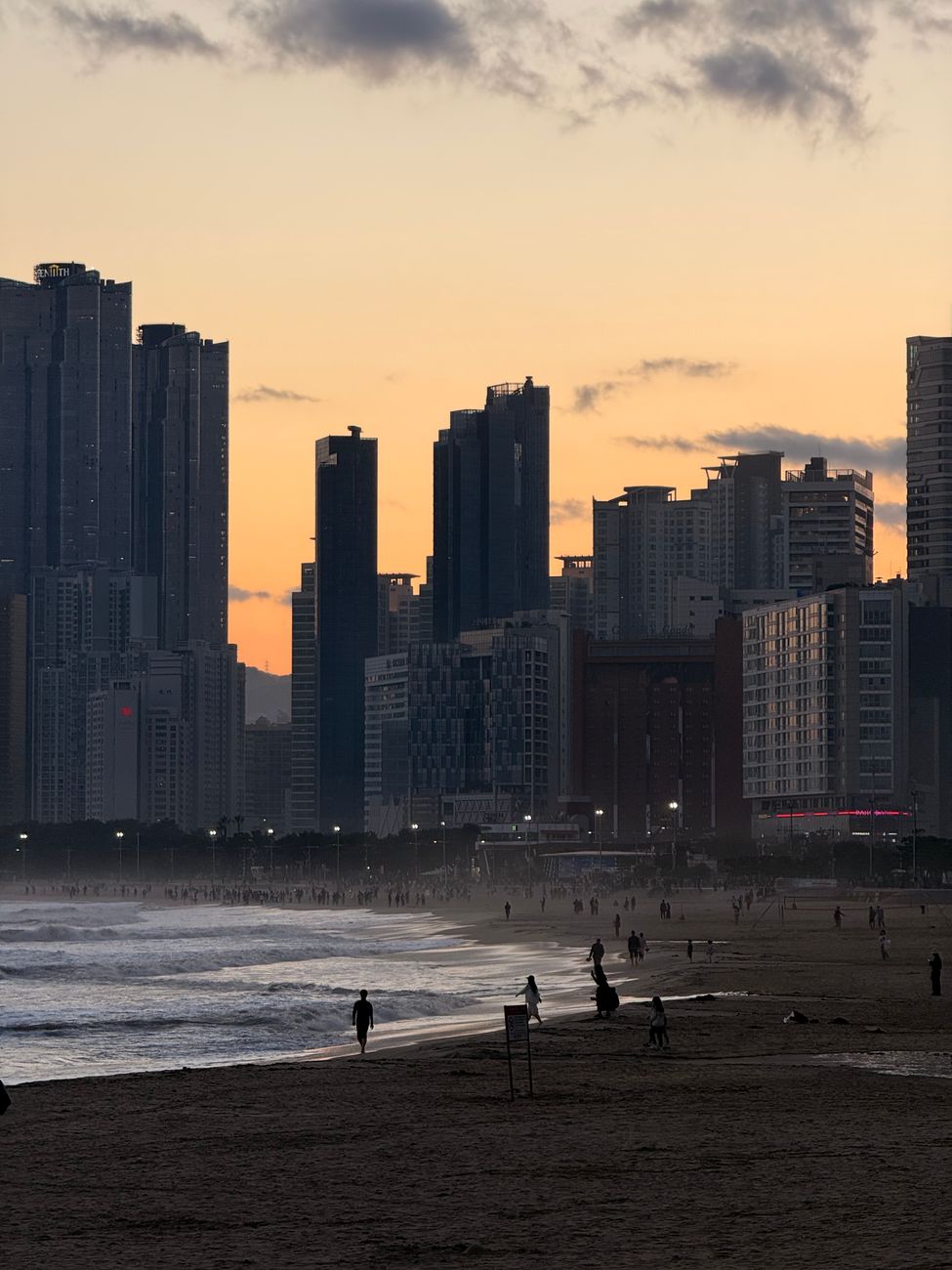 A serene view of Haeundae Beach at sunset with the Busan skyline.