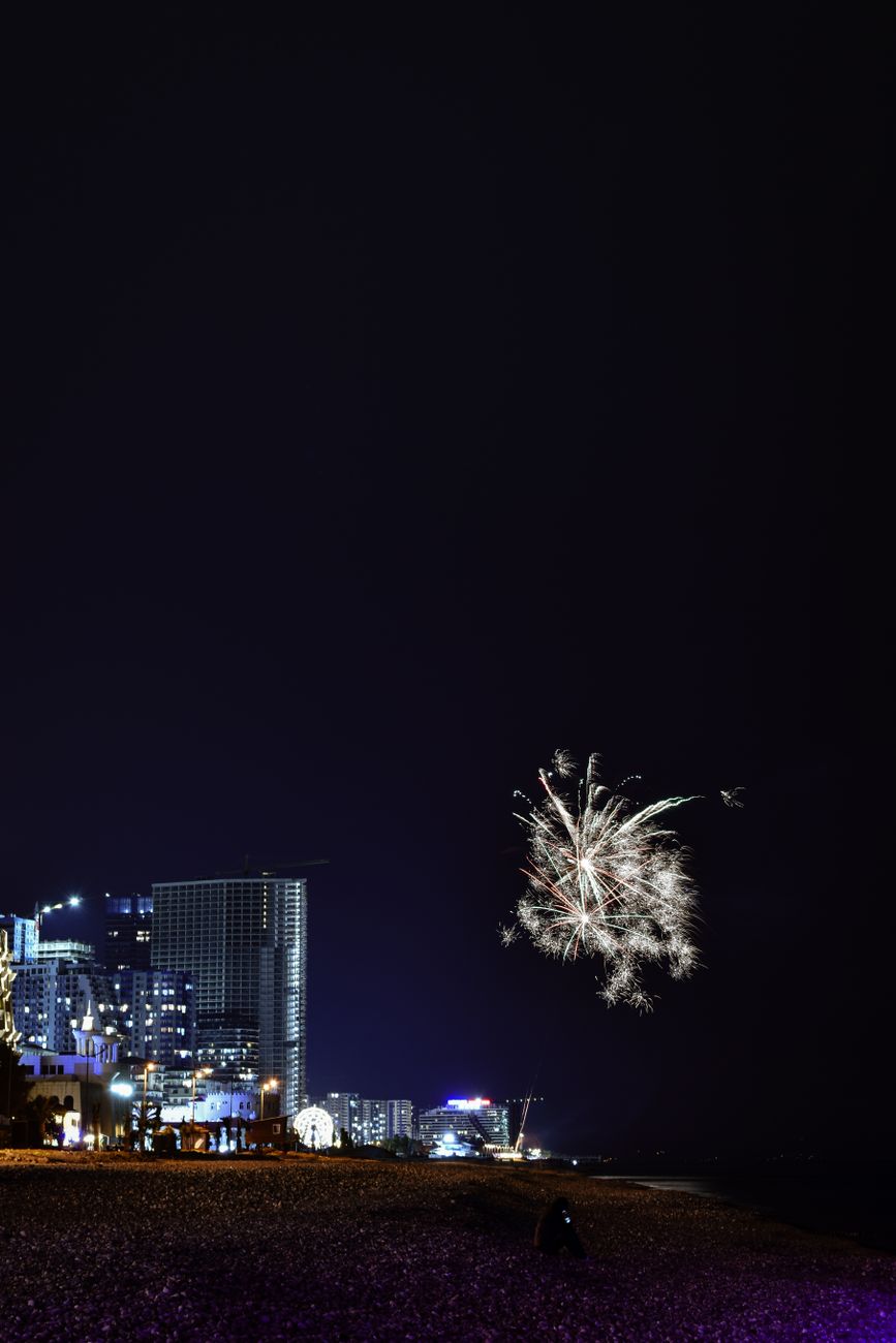 Vibrant fireworks light up a city skyline along the beach at night, celebrating a festive occasion.