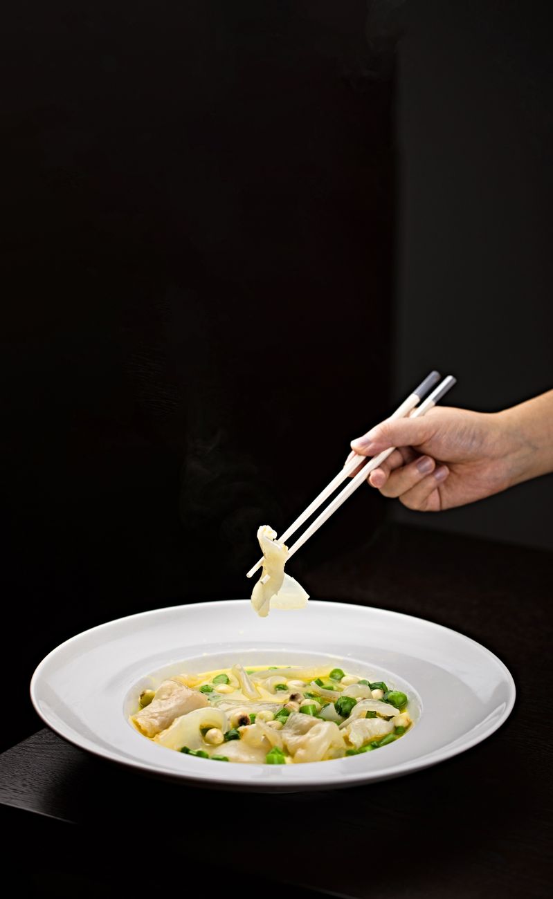 Asian dumpling noodle soup with vegetables being lifted by chopsticks in a close-up shot.