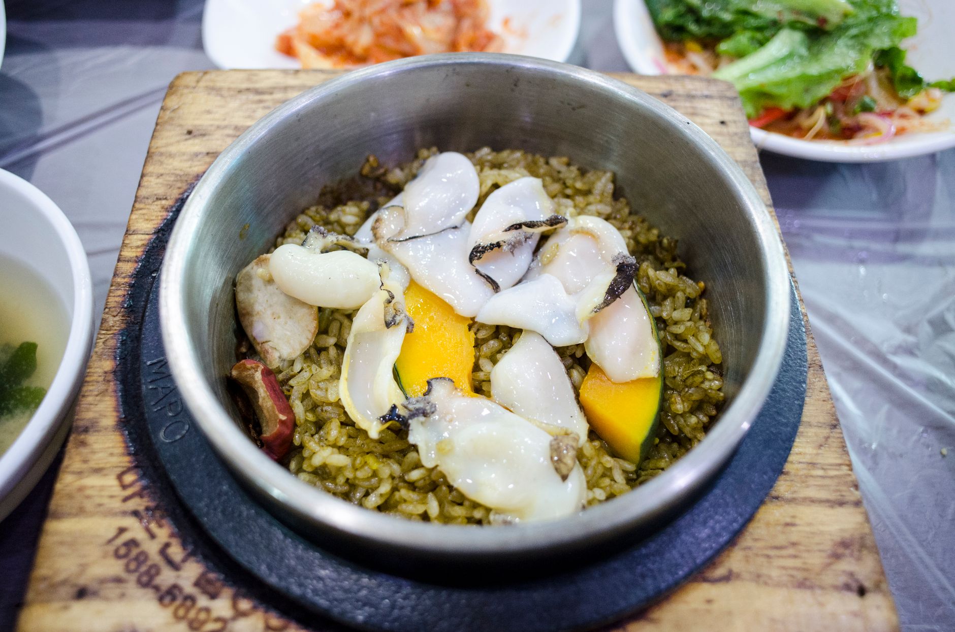 Close-up of a Korean abalone bibimbap dish with rice and vegetables in a hot pot, showcasing food styling.