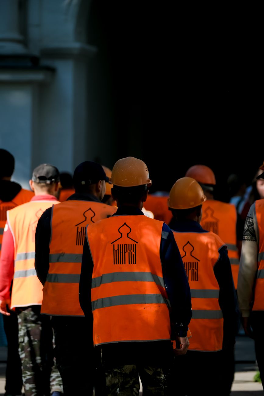 Group of construction workers with orange safety vests and helmets walking in Moscow.