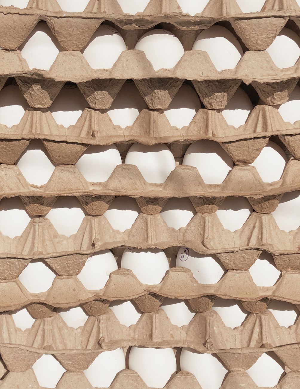 Stacked cardboard egg trays filled with white eggs viewed from above.