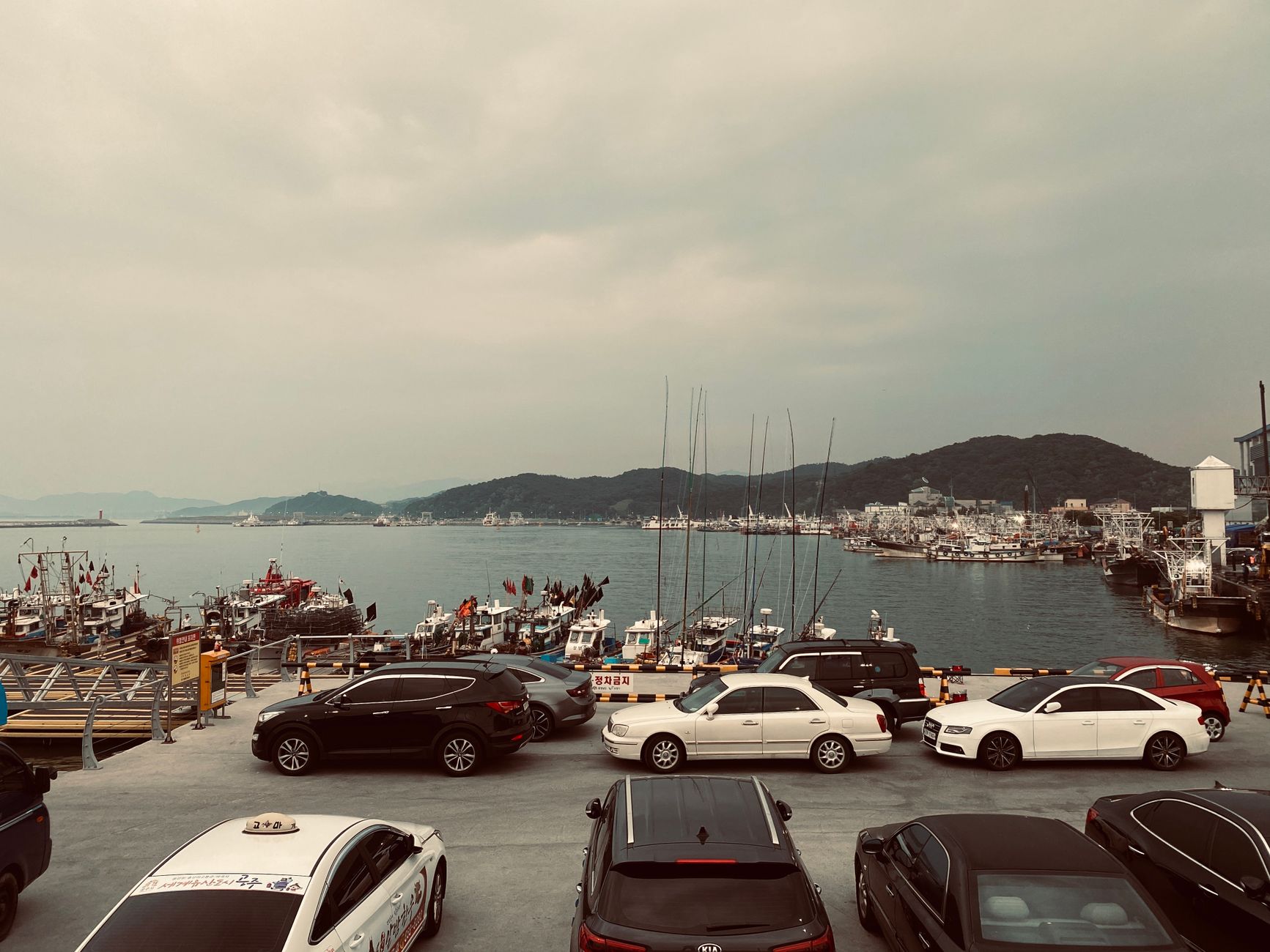 A quiet harbour on a southern Korean coast, with calm water backed by green mountains.
