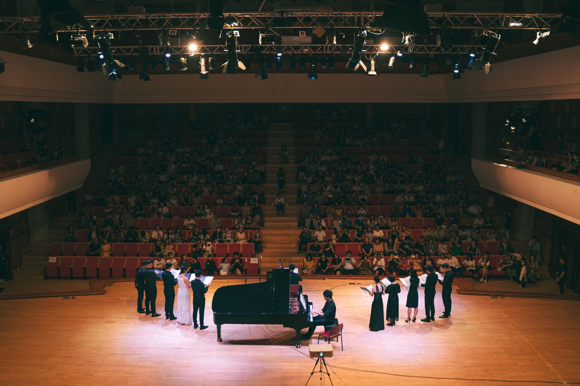 A live concert with a pianist and singers performing on a lit stage.