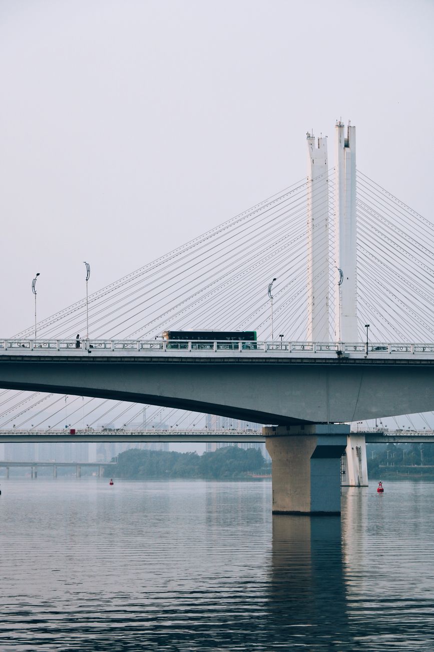 A modern suspension bridge with a bus crossing over a calm river, capturing urban transportation.
