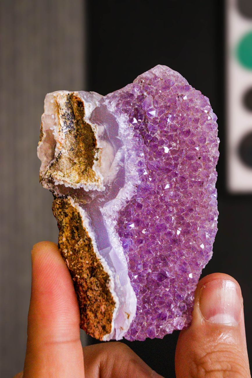 Detailed view of a purple amethyst geode crystal held between fingers, showcasing natural beauty.