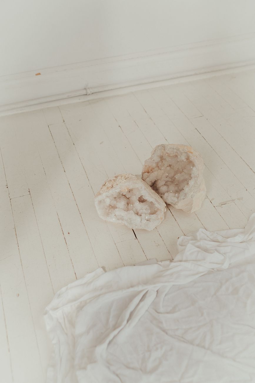 Elegant geode crystal displayed on a pale wooden floor with a subtle minimalist sheet.